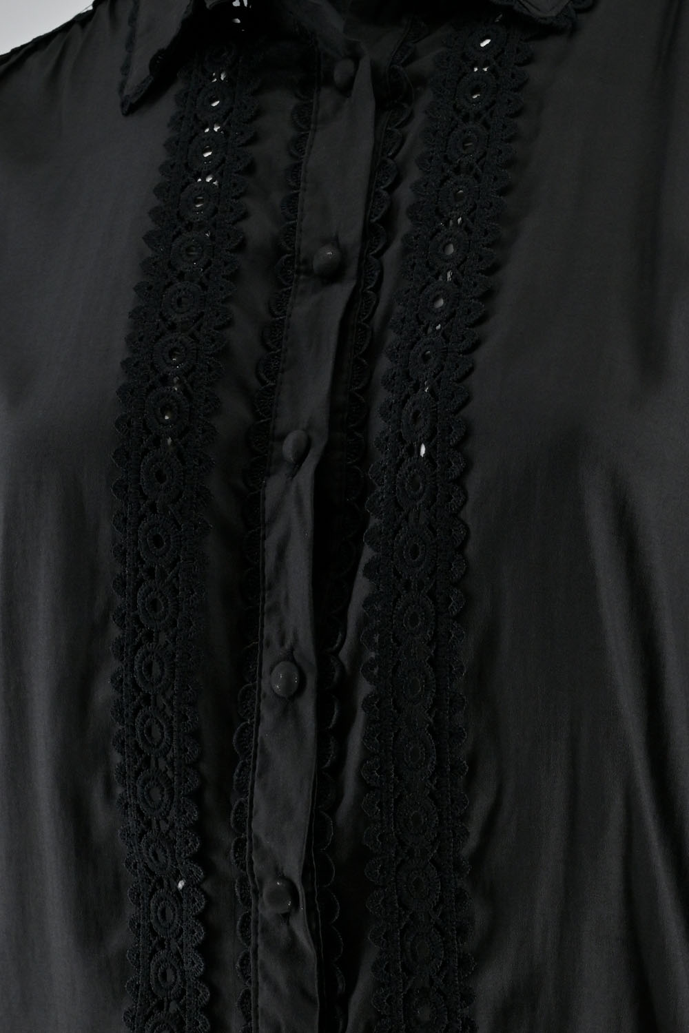Close-up of a black shirt featuring lace details along the button placket and collar.
