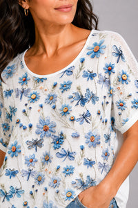 Λευκό γυναικείο T-shirt με γαλάζιο floral και dragonfly print, κοντό μανίκι και διάτρητες λεπτομέρειες στους ώμους.