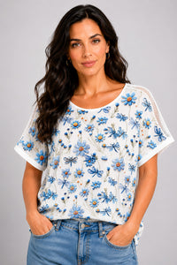 Λευκό γυναικείο T-shirt με γαλάζιο floral και dragonfly print, κοντό μανίκι και διάτρητες λεπτομέρειες στους ώμους.