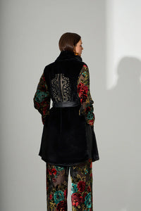 Αμάνικο μαύρο γυναικείο παλτό με ζώνη στη μέση και γιακά, φορεμένο σε μοντέλο σε studio φωτογράφιση