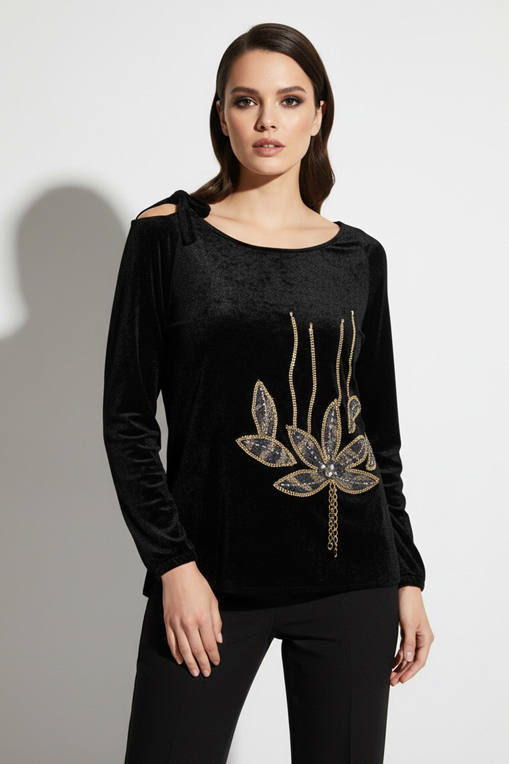 Μαύρη βελούδινη μπλούζα με χρυσό μοτίβο και φιόγκο στον ώμο, φορεμένη από μοντέλο σε studio.