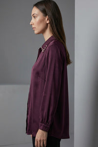 Μπορντό γυναικείο πουκάμισο με μεταλλικά τρουκς στον γιακά και μακρύ μανίκι, σε άνετη γραμμή.