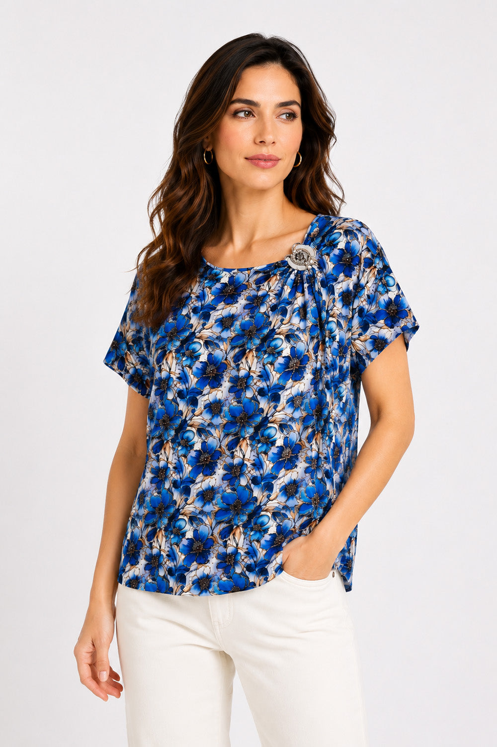 Εμπριμέ μπλούζα με μπλε floral print, κοντό μανίκι, στρογγυλή λαιμόκοψη και διακοσμητική καρφίτσα στον ώμο.