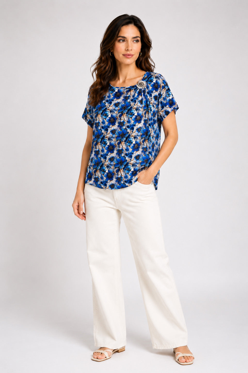 Εμπριμέ μπλούζα με μπλε floral print, κοντό μανίκι, στρογγυλή λαιμόκοψη και διακοσμητική καρφίτσα στον ώμο.
