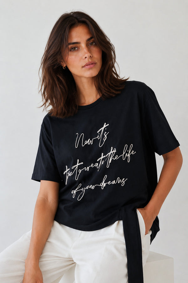 Γυναικείο μαύρο T-shirt με κεντημένο μήνυμα και διακοσμητική πλαϊνή κορδέλα στο τελείωμα.