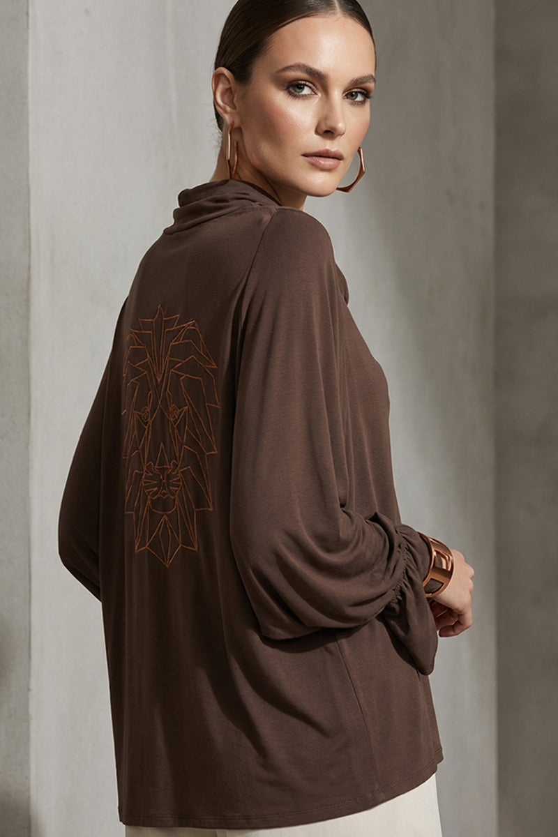 Καφέ μπλούζα ντραπέ με μακριά μανίκια και διακοσμητικό τύπωμα λιονταριού στην πλάτη, φορεμένη σε μοντέλο.