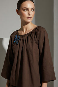 Καφέ γυναικεία μπλούζα με στρογγυλή λαιμόκοψη και κεντημένο μπλε φιόγκο στο στήθος.