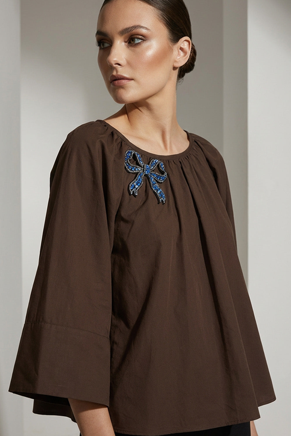 Καφέ γυναικεία μπλούζα με στρογγυλή λαιμόκοψη και κεντημένο μπλε φιόγκο στο στήθος.