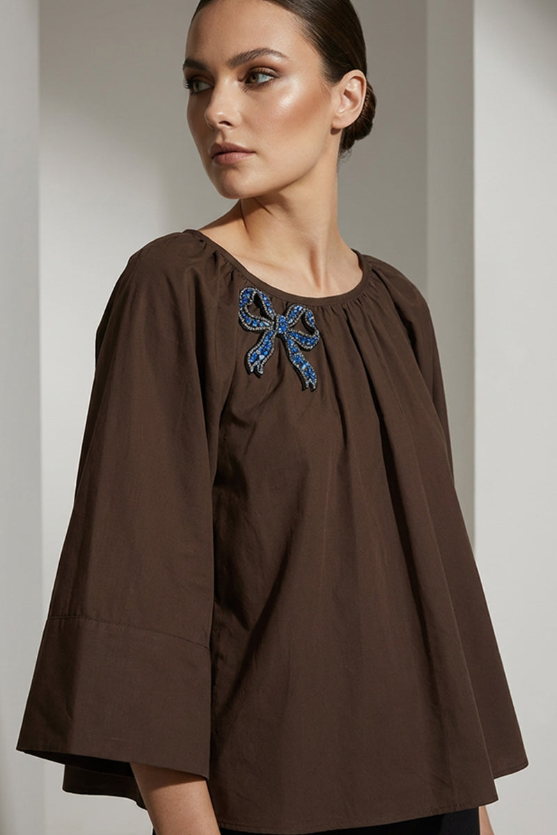 Καφέ γυναικεία μπλούζα με στρογγυλή λαιμόκοψη και κεντημένο μπλε φιόγκο στο στήθος.