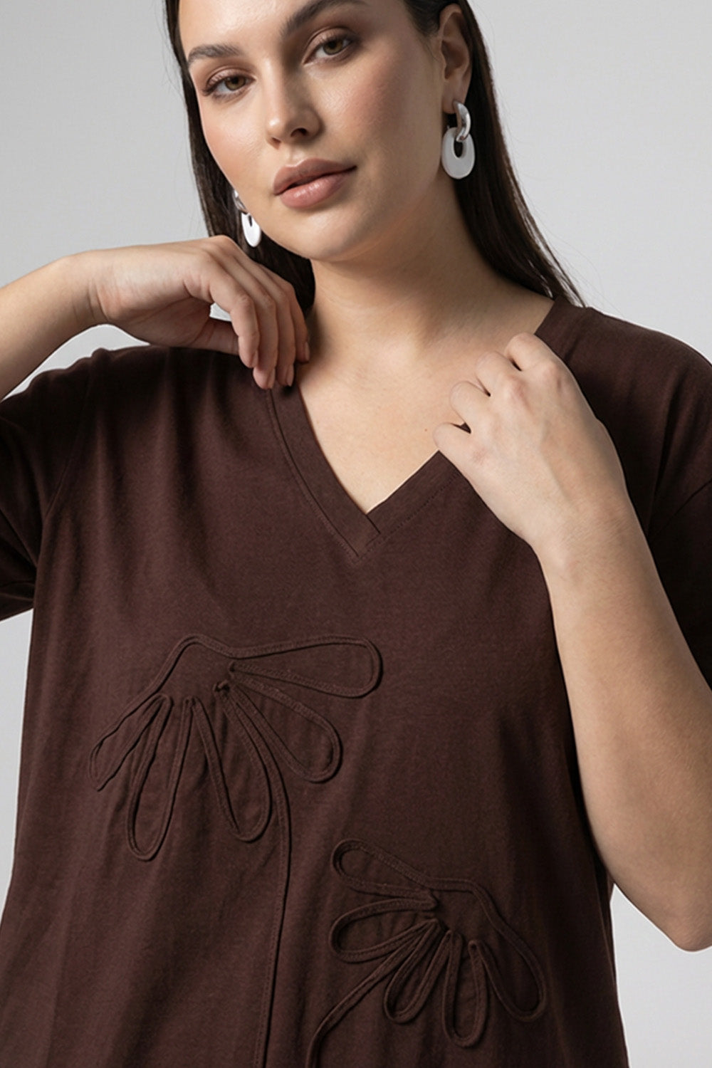 Καφέ oversized μπλούζα με V λαιμόκοψη και ανάγλυφα διακοσμητικά μοτίβα μπροστά.