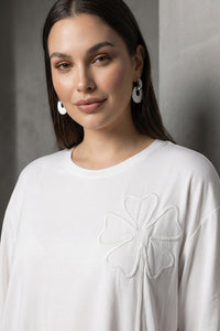 Λευκή oversized μπλούζα με ανάγλυφο λουλουδάτο σχέδιο στο στήθος και κοντά μανίκια.