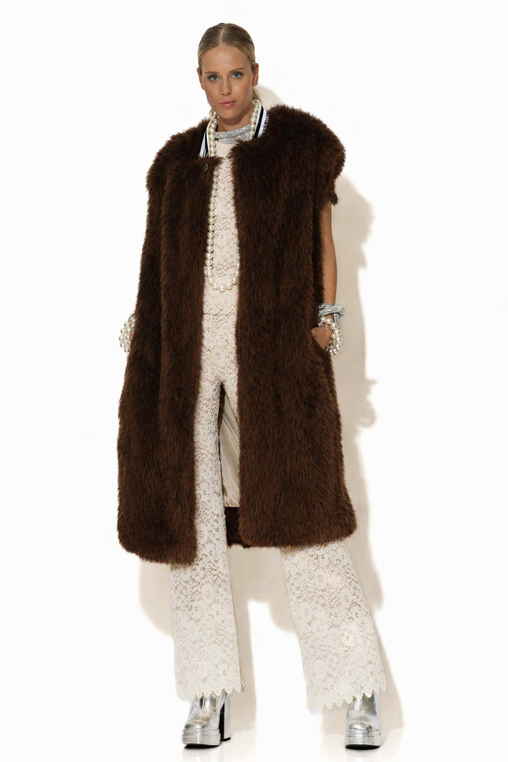 Μακρύ αμάνικο παλτό από συνθετική γούνα σε σκούρο καφέ χρώμα, με πλούσια υφή και ίσια γραμμή, φορεμένο σε κομψό σύνολο.