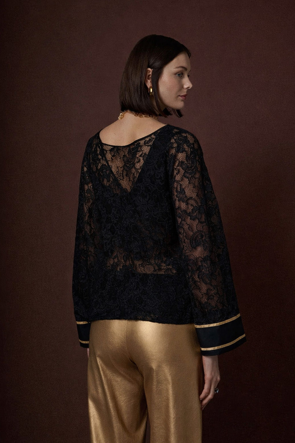 Μαύρη δαντελένια γυναικεία μπλούζα με διαφάνεια και χρυσή λεπτομέρεια στα μανίκια, φορεμένη από μοντέλο.