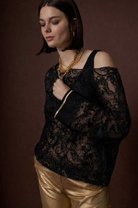 Μαύρη δαντελένια γυναικεία μπλούζα με διαφάνεια και χρυσή λεπτομέρεια στα μανίκια, φορεμένη από μοντέλο.