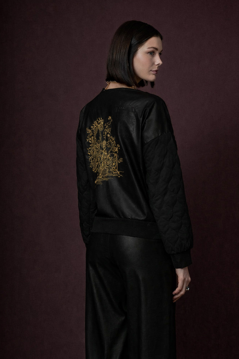 Μαύρη καπιτονέ μπλούζα γυναικεία με χρυσό κέντημα στην πλάτη, φωτογραφημένη σε studio με μοντέλο