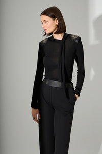 Μαύρη γυναικεία μπλούζα με μακριά μανίκια, χρυσές λεπτομέρειες στους ώμους και δέσιμο στον λαιμό, φορεμένη σε μοντέλο σε studio φωτογράφιση