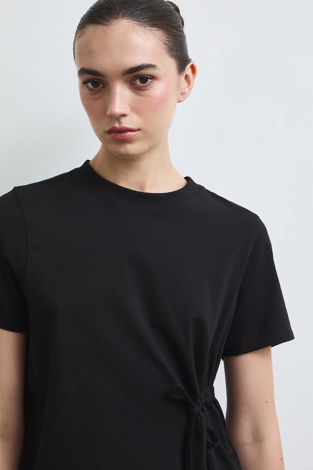 Γυναικείο μαύρο T-shirt με πλαϊνή σούρα, κορδόνι στη μέση και ασύμμετρο τελείωμα, συνδυασμένο με πουά φούστα.