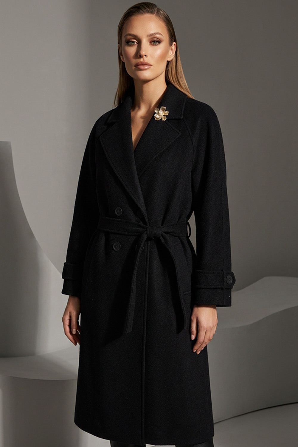 Μαύρο παλτό με ζώνη στη μέση και διακοσμητική καρφίτσα, φορεμένο από μοντέλο.