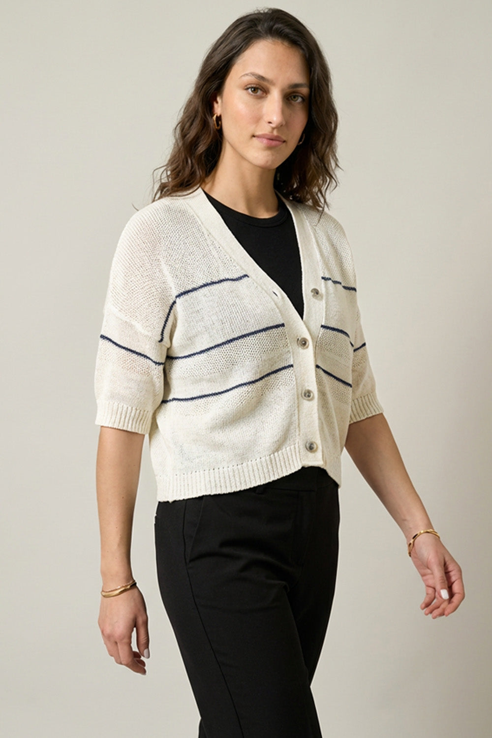 Πλεκτή κοντομάνικη ζακέτα σε εκρού χρώμα με λεπτές οριζόντιες ρίγες, V ντεκολτέ και κουμπιά μπροστά, σε ίσια γραμμή.