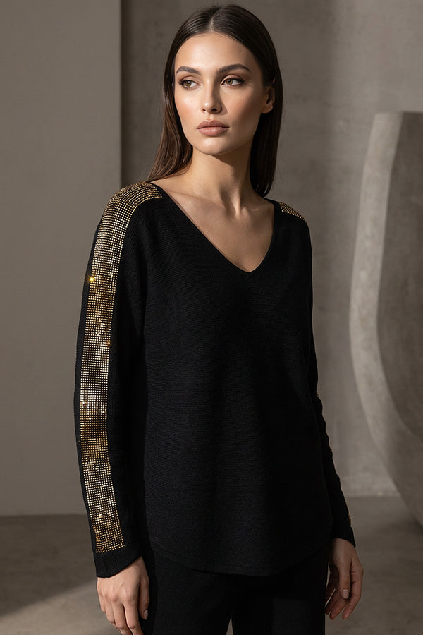 Μαύρη πλεκτή μπλούζα με V λαιμόκοψη και χρυσές λεπτομέρειες στους ώμους και μανίκια, φορεμένη από μοντέλο studio.