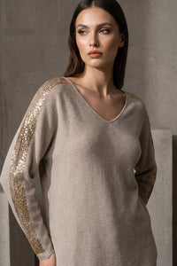 Μπεζ πλεκτή μπλούζα με V λαιμόκοψη και χρυσές λεπτομέρειες σε ώμους και μανίκια, φορεμένη από μοντέλο studio.