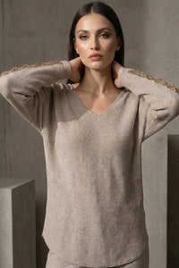 Μπεζ πλεκτή μπλούζα με V λαιμόκοψη και χρυσές λεπτομέρειες σε ώμους και μανίκια, φορεμένη από μοντέλο studio.