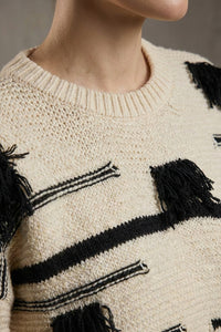Εκρού πλεκτή μπλούζα με μαύρες ρίγες και διακοσμητικά κρόσσια, φορεμένη από μοντέλο σε studio φόντο.