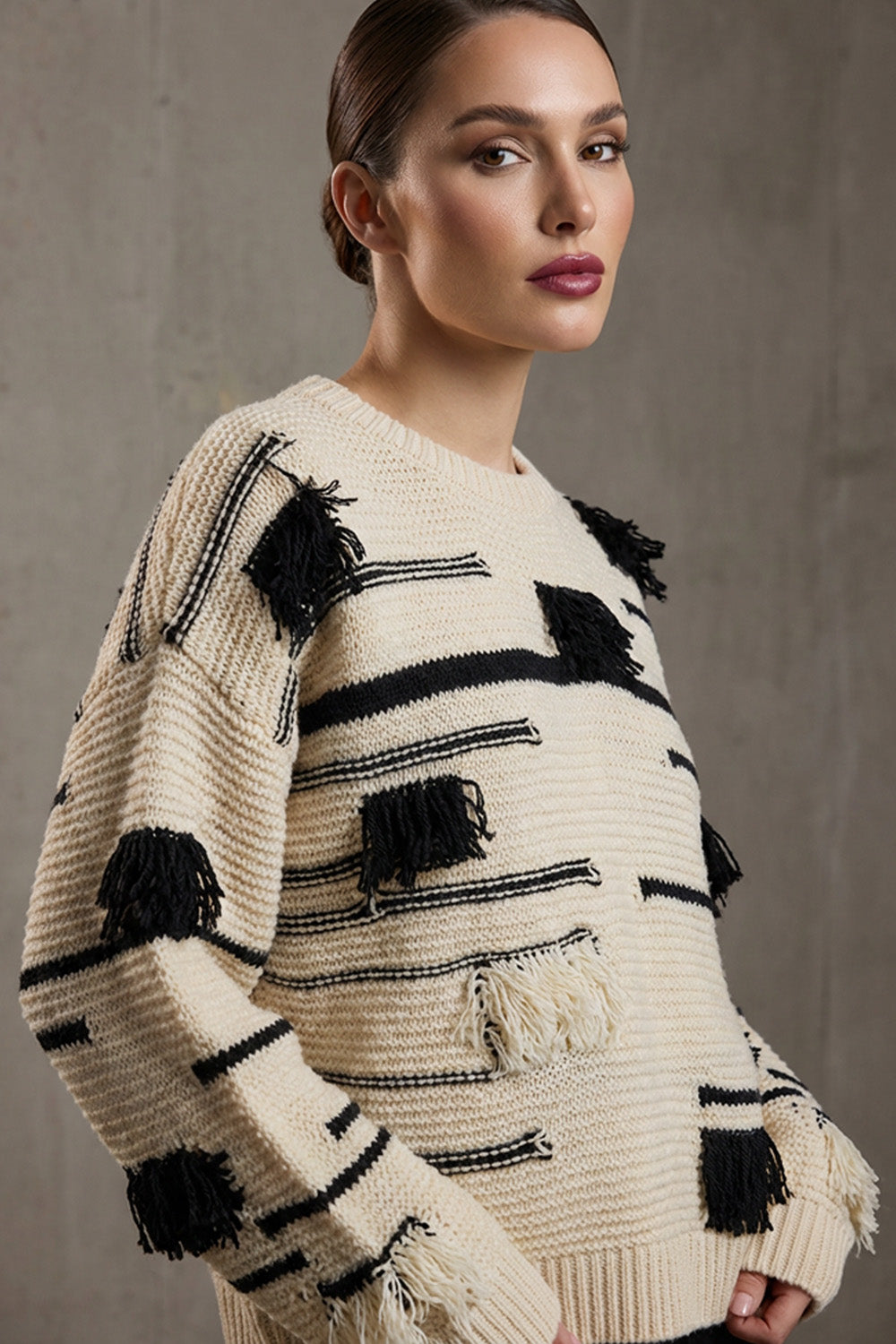 Εκρού πλεκτή μπλούζα με μαύρες ρίγες και διακοσμητικά κρόσσια, φορεμένη από μοντέλο σε studio φόντο.