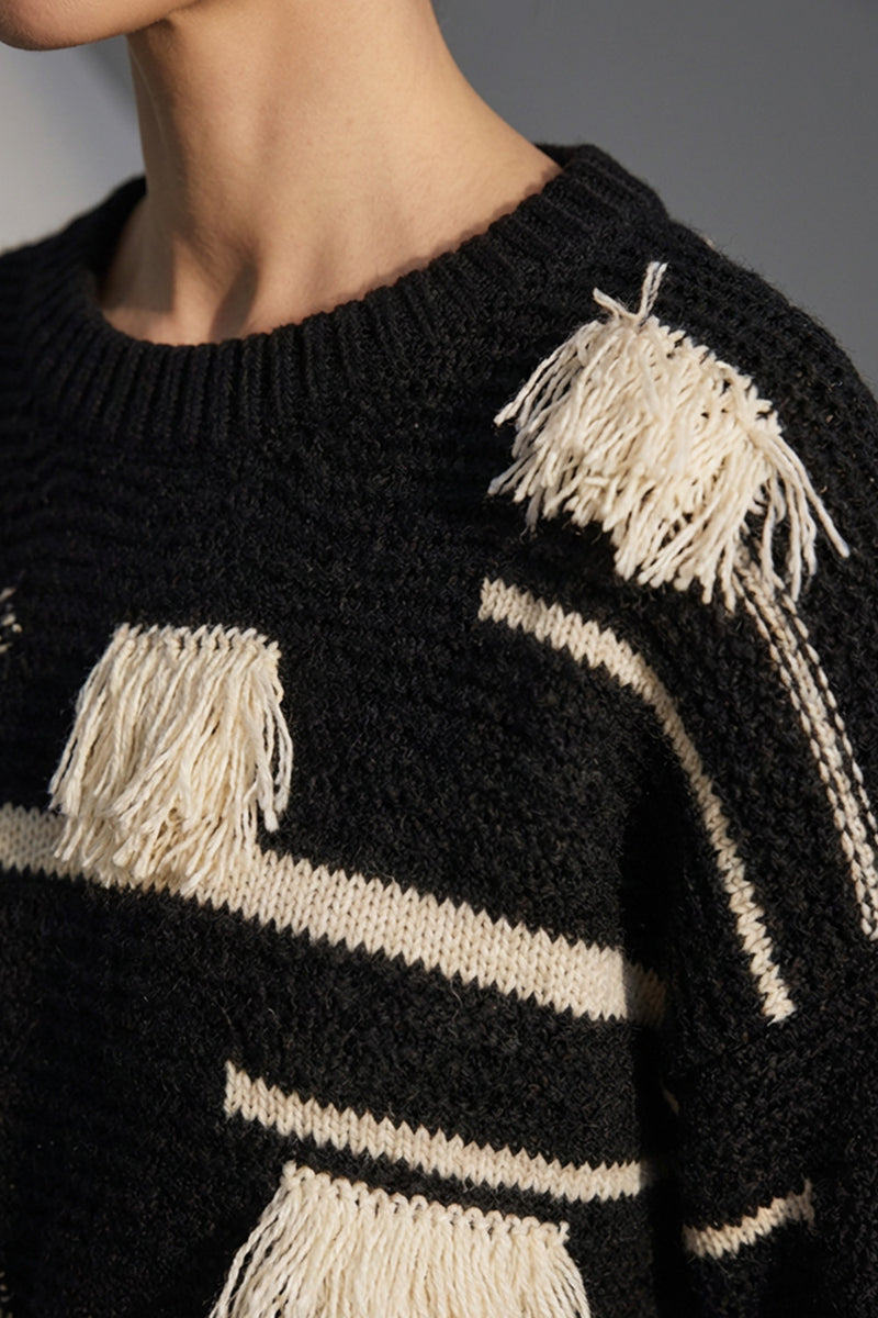 Μαύρη πλεκτή μπλούζα με εκρού ρίγες και διακοσμητικά κρόσσια, φορεμένη από μοντέλο σε studio φόντο.