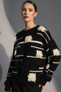 Μαύρη πλεκτή μπλούζα με εκρού ρίγες και διακοσμητικά κρόσσια, φορεμένη από μοντέλο σε studio φόντο.