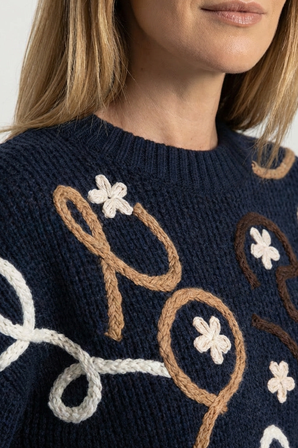 Πλεκτή navy μπλούζα με κεντημένο ανάγλυφο σχέδιο σε εκρού και καφέ, μακριά μανίκια και στρογγυλή λαιμόκοψη, φορεμένη από μοντέλο.