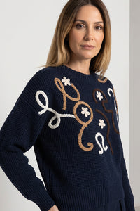 Πλεκτή navy μπλούζα με κεντημένο ανάγλυφο σχέδιο σε εκρού και καφέ, μακριά μανίκια και στρογγυλή λαιμόκοψη, φορεμένη από μοντέλο.