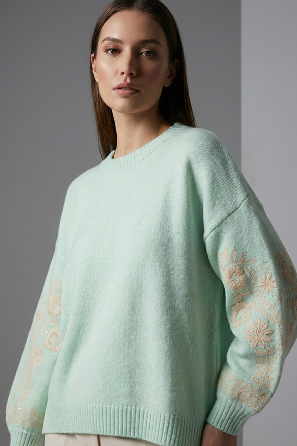 Πλεκτή mint μπλούζα με στρογγυλή λαιμόκοψη, μακρύ μανίκι με κεντημένο floral μοτίβο και άνετη γραμμή, φορεμένη με ανοιχτόχρωμο παντελόνι.