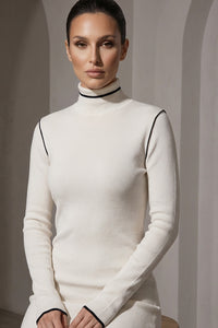 Πλεκτή εκρού μπλούζα με ψηλό γιακά και λεπτές μαύρες λεπτομέρειες αντίθεσης, φορεμένη από μοντέλο.