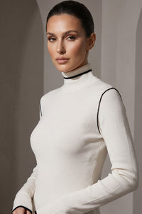 Πλεκτή εκρού μπλούζα με ψηλό γιακά και λεπτές μαύρες λεπτομέρειες αντίθεσης, φορεμένη από μοντέλο.