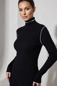 Πλεκτή μαύρη μπλούζα με ψηλό γιακά και λευκές λεπτομέρειες αντίθεσης, φορεμένη από μοντέλο.