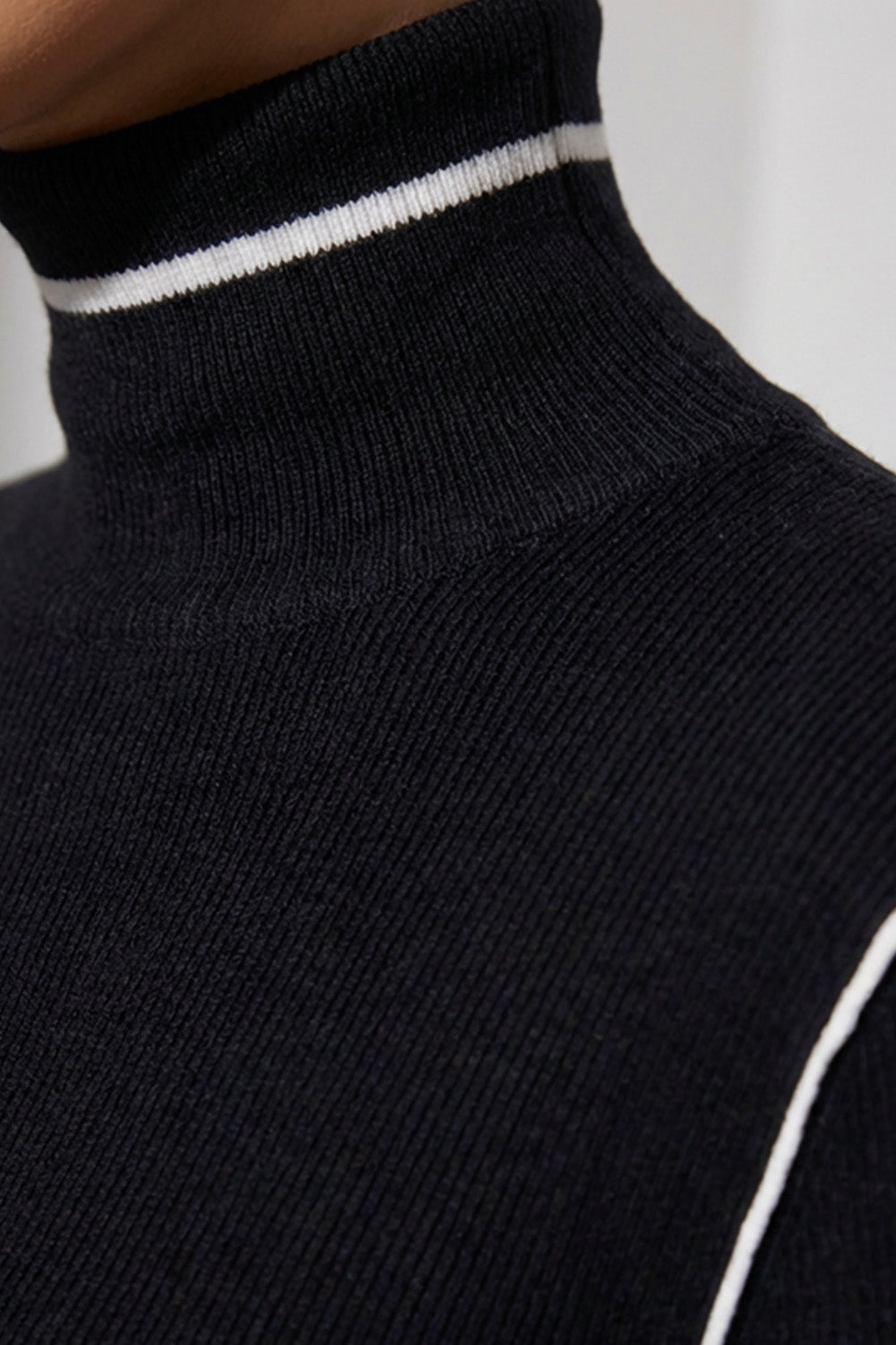 Πλεκτή μαύρη μπλούζα με ψηλό γιακά και λευκές λεπτομέρειες αντίθεσης, φορεμένη από μοντέλο.
