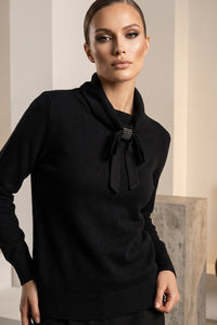 Μαύρη πλεκτή μπλούζα με φιόγκο στον λαιμό και μεταλλική διακοσμητική λεπτομέρεια, φορεμένη από μοντέλο σε minimal studio σκηνικό.