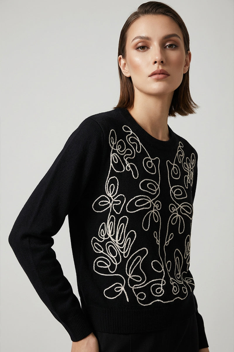 Μαύρη πλεκτή μπλούζα με εκρού κεντημένο καλλιτεχνικό σχέδιο στο μπροστινό μέρος, φορεμένη από μοντέλο σε minimal studio περιβάλλον.