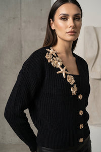 Πλεκτή μαύρη ζακέτα με διακοσμητικά μεταλλικής όψης στο μπροστινό μέρος, φορεμένη από μοντέλο.