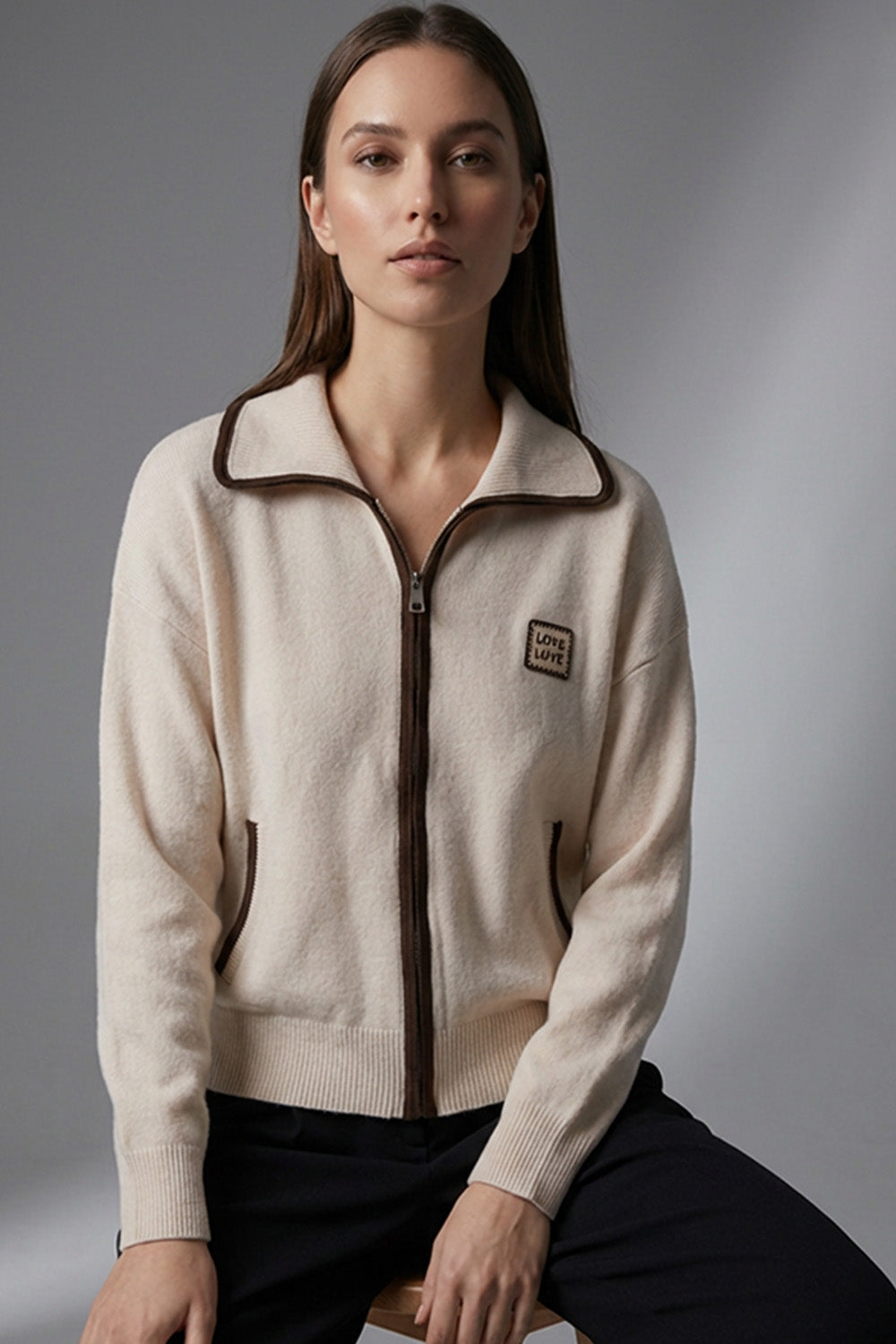 Γυναικεία εκρού πλεκτή ζακέτα με φερμουάρ, καφέ λεπτομέρειες και άνετη γραμμή, φορεμένη σε μοντέλο σε studio φόντο