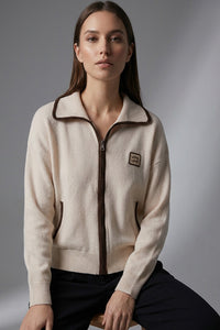 Γυναικεία εκρού πλεκτή ζακέτα με φερμουάρ, καφέ λεπτομέρειες και άνετη γραμμή, φορεμένη σε μοντέλο σε studio φόντο