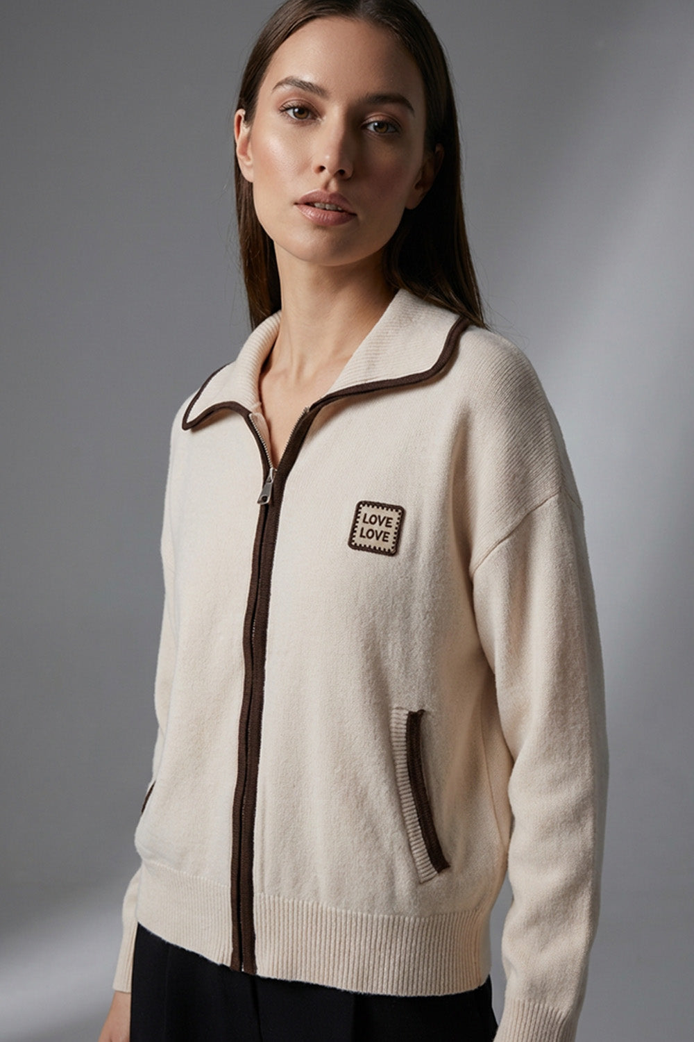 Γυναικεία εκρού πλεκτή ζακέτα με φερμουάρ, καφέ λεπτομέρειες και άνετη γραμμή, φορεμένη σε μοντέλο σε studio φόντο