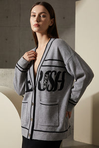 Πλεκτή γκρι ζακέτα με μαύρες λεπτομέρειες και lettering στο μπροστινό μέρος, φορεμένη από μοντέλο.