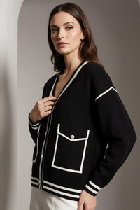 Μαύρη πλεκτή ζακέτα με λευκά τελειώματα, V λαιμόκοψη και διακοσμητικές τσέπες, φορεμένη από μοντέλο.