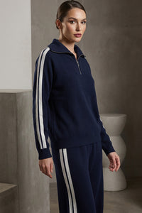 Μπλε πλεκτό σετ με λευκές ρίγες σε μανίκια και παντελόνι, με φερμουάρ στον λαιμό, φορεμένο από μοντέλο studio.