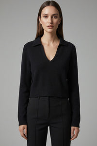 Μαύρη πλεκτή μπλούζα με γιακά, V λαιμόκοψη, μακρύ μανίκι και ριμπ τελείωμα, φορεμένη με μαύρο παντελόνι.