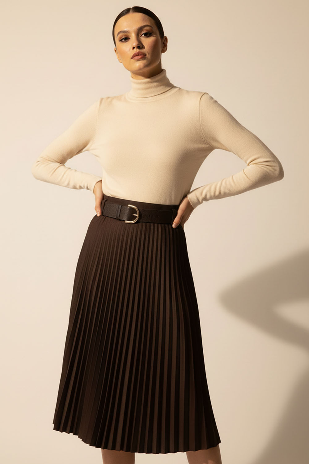 Καφέ πλισέ μίντι φούστα με ζώνη και αγκράφα σε στούντιο φωτογράφιση