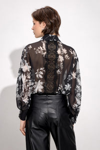 Γυναικεία μαύρη φλοράλ πουκαμίσα με διακοσμητικό φιόγκο και μακριά μανίκια, φορεμένη με μαύρο παντελόνι.