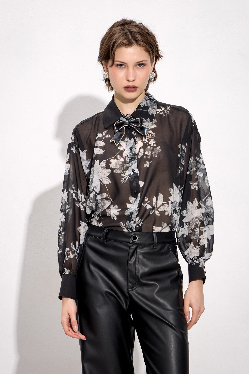 Γυναικεία μαύρη φλοράλ πουκαμίσα με διακοσμητικό φιόγκο και μακριά μανίκια, φορεμένη με μαύρο παντελόνι.